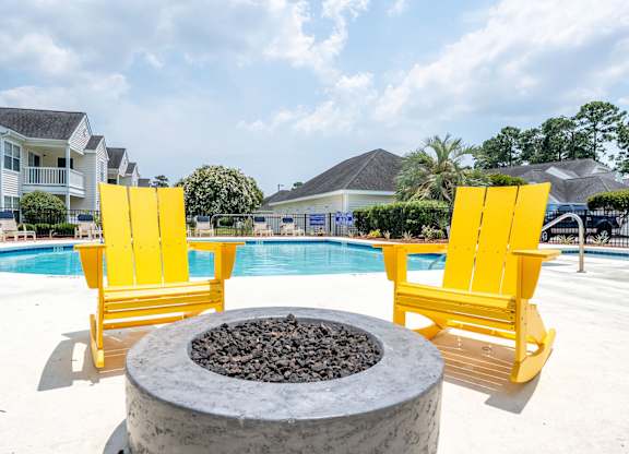 Two yellow chairs are placed on a patio next to a fire pit.