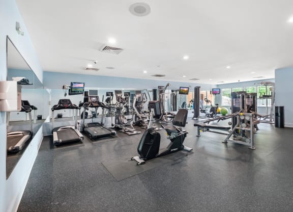 a spacious fitness room with cardio equipment and flat screen tvs