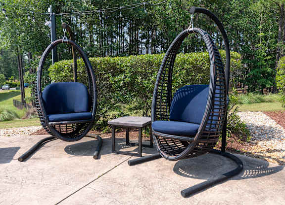 Two hanging chairs with blue cushions are placed in a garden.