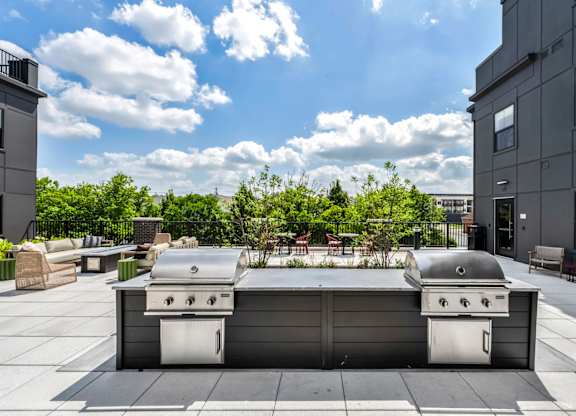 A grill is on a patio with a building in the background.