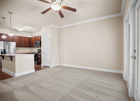 an empty living room with a ceiling fan and a kitchen