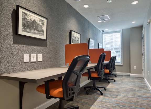 A row of orange chairs are lined up in front of a white desk.