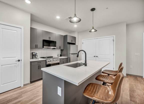 A modern kitchen with a large island and brown chairs.