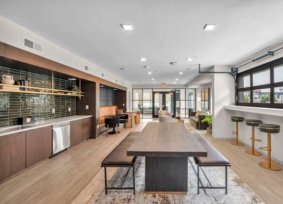 A modern kitchen with a long wooden table in the middle.