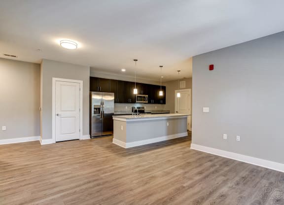 an empty living room with a kitchen with a refrigerator and a sink at Barclay Place Apartments, North Carolina