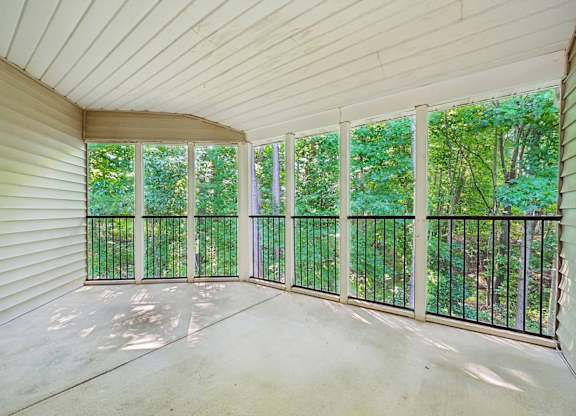 A sunny day in a room with a balcony overlooking a green forest.