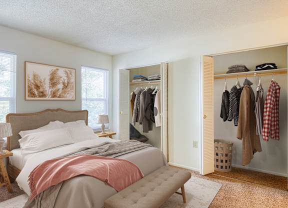 A bedroom with a bed, a clothing rack, and a painting on the wall at The Everett  Apartments in Roanoke, 24018