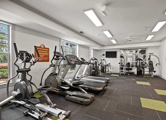A gym with a variety of equipment including treadmills, weights, and a television.