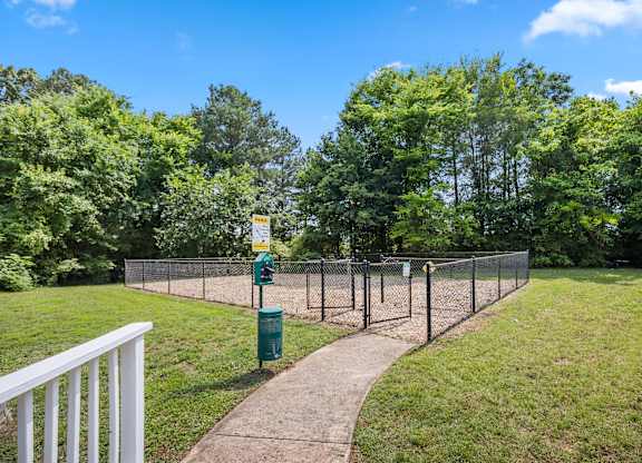 A green trash can sits on a concrete path next to a chain link fence.