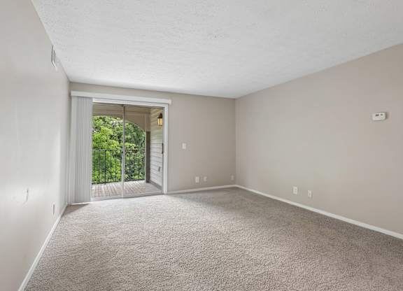 A room with a carpeted floor and a sliding glass door leading to a balcony.