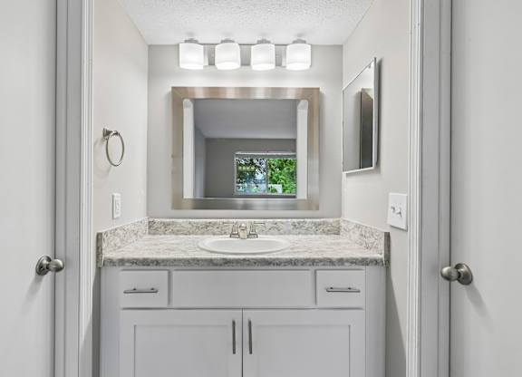 A bathroom with a sink, mirror, and cabinets.