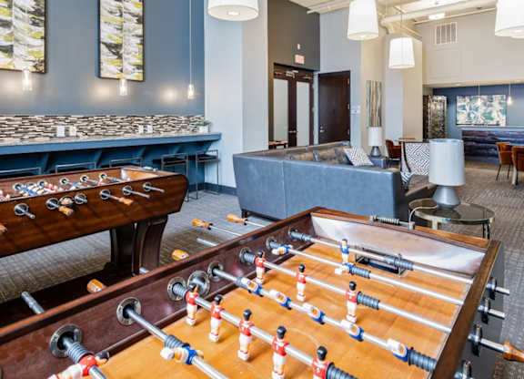 A foosball table is in the middle of a room with a pool table and couches.