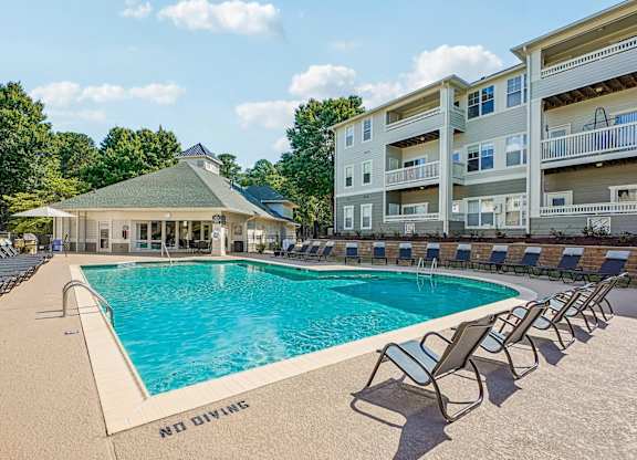 A pool with chairs around it and a building in the background.