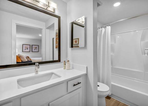 A white bathroom with a sink, mirror, and bathtub.