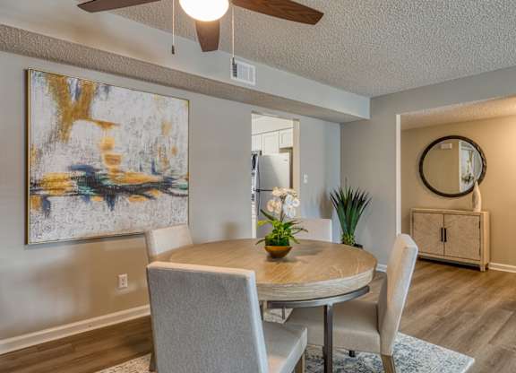 A dining room with a table and chairs and a painting on the wall.