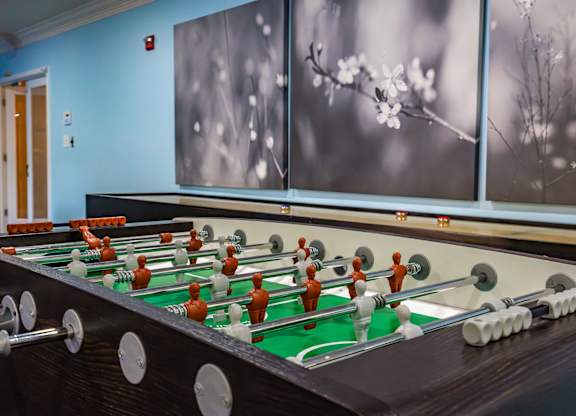 A foosball table is in the middle of a room with a blue wall and two framed pictures on it.