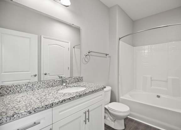 A white bathroom with a granite countertop and a white bathtub.