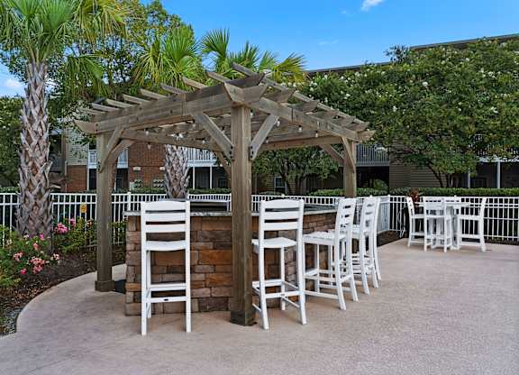 A wooden pergola with white chairs is surrounded by a garden at Litchfield Oaks Apartments in SC, 29585