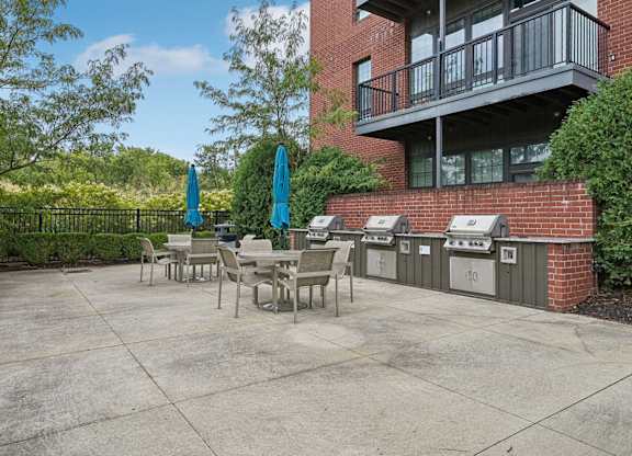A patio with a table and chairs is surrounded by a brick building and trees.