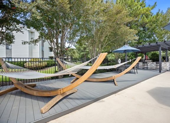 two hammocks on a patio with umbrellas and trees