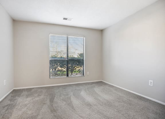 an empty living room with a window and carpeting