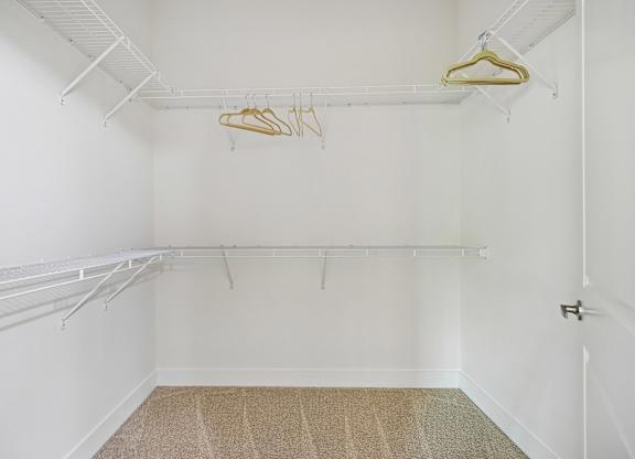 A white closet with a carpeted floor and a few clothes hanging on a hanger.
