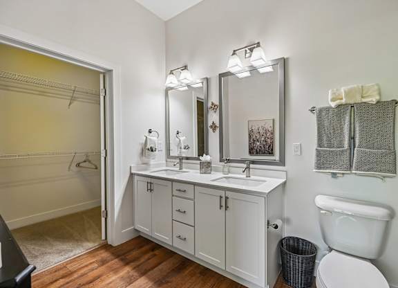 A bathroom with a white toilet, a sink with a mirror above it, and a towel rack with towels hanging on it.