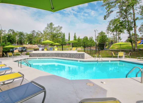 our resort style swimming pool is filled with lounge chairs and umbrellas