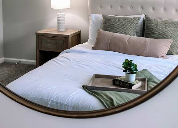 A bedroom with a bed, a nightstand with a lamp, and a painting on the wall.