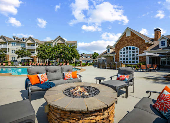 A fire pit sits in the middle of a patio surrounded by chairs and cushions.