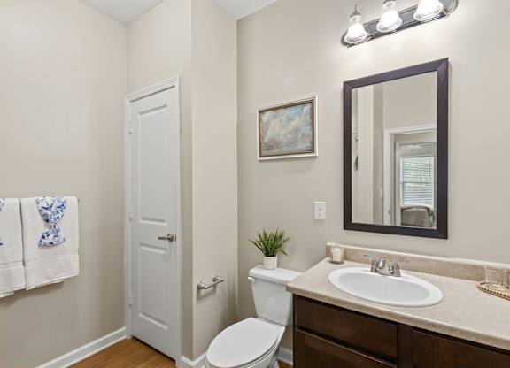 A bathroom with a toilet, sink, mirror, and a door.