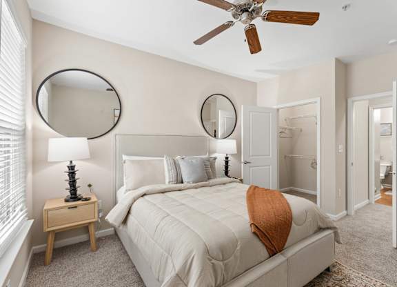 A bedroom with a large bed, a ceiling fan, and two round mirrors on the wall.