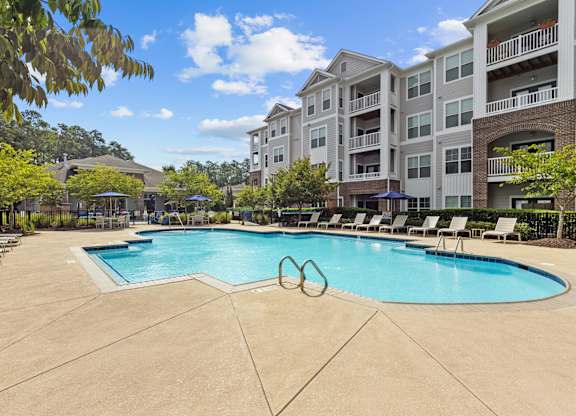 A large swimming pool surrounded by lounge chairs and apartment buildings.