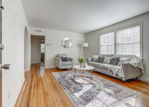 A living room with a grey couch and a round table with a vase of flowers on it.