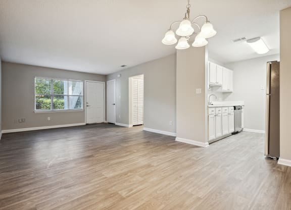 an empty living room with a kitchen in the background