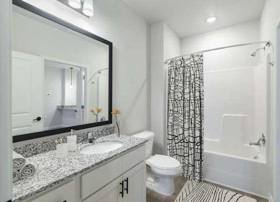 A bathroom with a sink, mirror, toilet, and shower.
