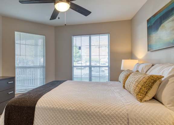A bedroom with a large bed, a ceiling fan, and a view of the city.