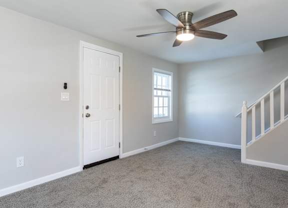 A room with a ceiling fan and a staircase.