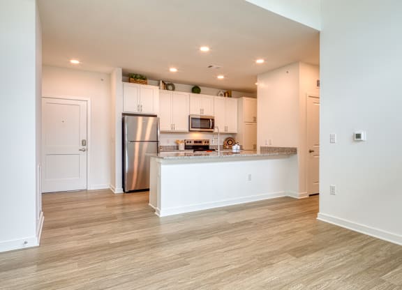 an open kitchen and living room with white cabinets and a stainless steel refrigerator at Allure at Edinburgh, Virginia