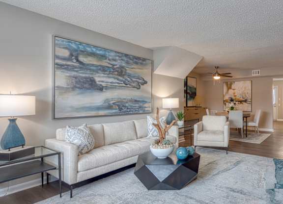 A living room with a large painting on the wall and a white couch.