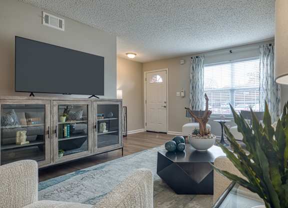 A living room with a flat screen TV and a glass table.