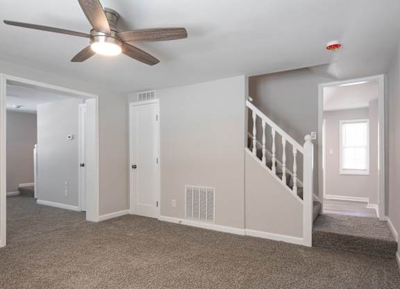 A room with a ceiling fan and a staircase.