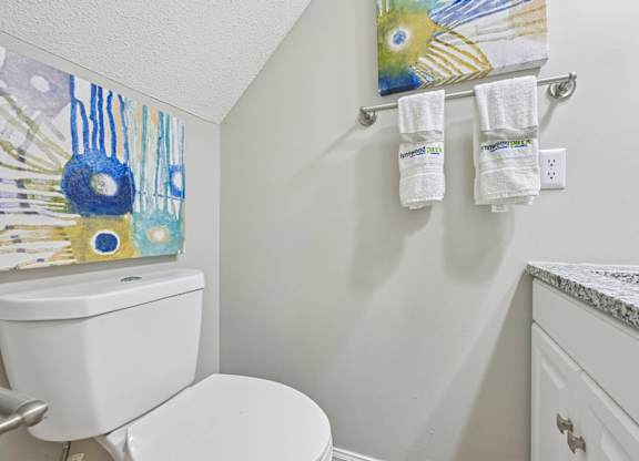 A white toilet in a bathroom with a painting on the wall.