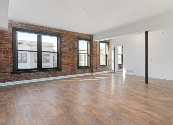 an empty living room with a brick wall and wood floors at The Madison, Columbus