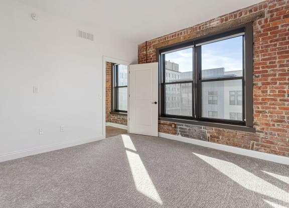 an empty living room with a brick wall and a large window at The Madison, Columbus, 43215