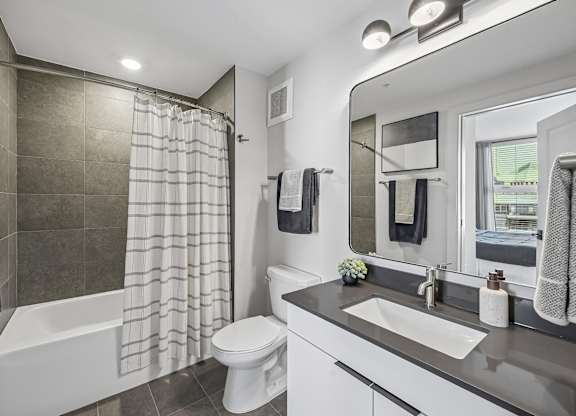 A modern bathroom with a white toilet, a bathtub with a shower curtain, a sink, and a mirror.