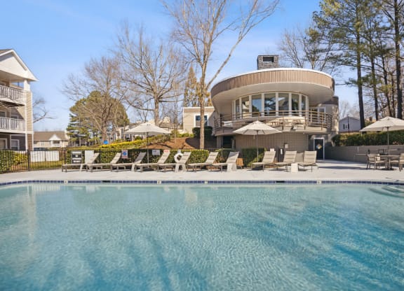 a swimming pool with chairs and a house in the background