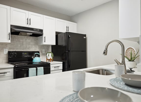 a kitchen with white cabinets and a sink and black refrigerator