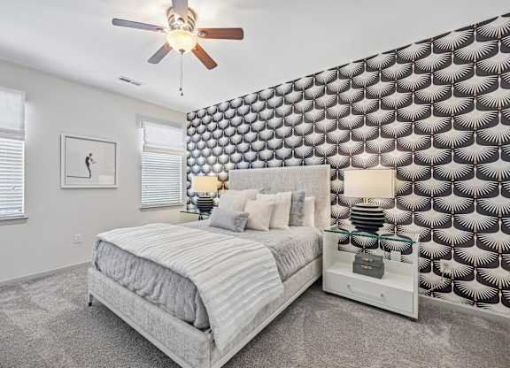A bedroom with a bed, a ceiling fan, and a patterned wallpaper.