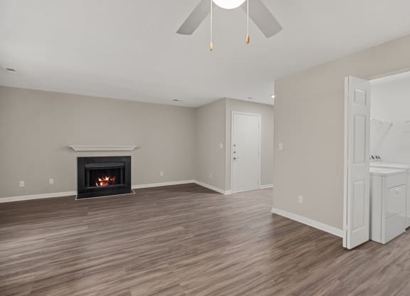 an empty living room with a fireplace and a white kitchen